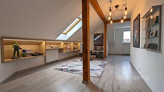 Podkrovní místnost s dřevěnými trámy, moderní osvětlení, světlá laminátová podlaha, vestavěné police, stylová a prostorná pro různé využití.