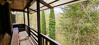 Krytá terasa s dřevěnými prvky a výhledem na zahradu, okolní stromy a přírodní prostředí, poskytuje klidné místo k posezení.