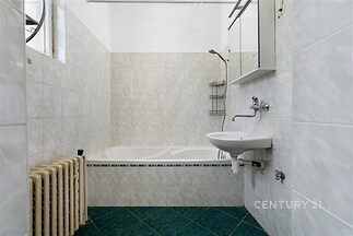 Koupelna s keramickými obklady, zelenou dlažbou a vanou, zrcadlová skříňka nad umyvadlem, dobře udržovaný stav.