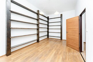 Prázdná místnost s dřevěnou parketovou podlahou, vysoké regály a moderní design. Světlý prostor vhodný pro knihovnu nebo osobní kancelář.