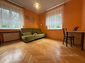 Světlý obývací pokoj s parketovou podlahou, velkými okny a moderním nábytkem.