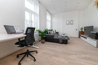 Světlý obývací pokoj s parketovou podlahou, moderní nábytkem a velkými okny. Elegantní bílá stěna doplňuje vzdušný prostor.