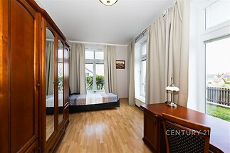 Světlá ložnice s parketovou podlahou, velkými okny a dřevěným nábytkem, působí moderně a prostorně.