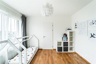 Dětský pokoj s moderním nábytkem, parketovou podlahou a velkými okny, zajišťuje dostatek přirozeného světla.