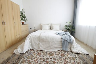 Prostorná ložnice s parketovou podlahou, velkými okny a světlou výmalbou, doplněná moderním nábytkem a dekorativním kobercem.