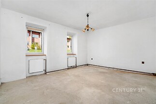 Prázdná světlá místnost, betonová podlaha, bílá výmalba, dvě okna s výhledem na zeleň, příprava na rekonstrukci, ideální pro modernizaci