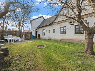 Zahrada s trávníkem u rodinného domu, oplocená dřevěným plotem, s venkovním posezením a ohništěm, klidné prostředí pro relaxaci.