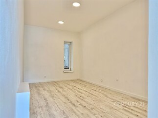 Prázdný pokoj s moderní vinylovou podlahou, bílými stěnami a vysokým stropem, ideální pro rekonstrukci a přizpůsobení podle vlastního stylu.