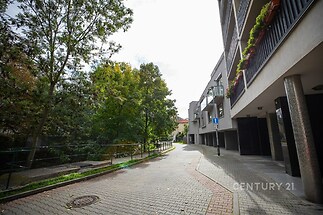 Moderní bytový komplex s balkonem, obklopený zelení a zpevněnou příjezdovou cestou, nabízí klidné prostředí a kvalitní městské bydlení.
