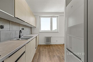 Moderní kuchyň s parketovou podlahou a vestavěnými skříněmi, velká okna zajišťují světlé a vzdušné prostředí.