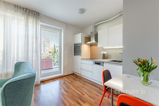 Světlý obývací pokoj s moderní kuchyní, parketová podlaha, velká okna, elegantní nábytek, moderní design, příjemná atmosféra.