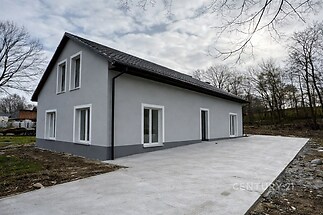 Novostavba rodinného domu s moderní fasádou, betonová příjezdová cesta, velká francouzská okna, klidná lokalita v přírodě.