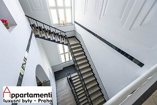 Světlé schodiště s velkými okny, elegantní zábradlí a moderní design, bílá omítka a přírodní materiály dodávají prostornost a eleganci.