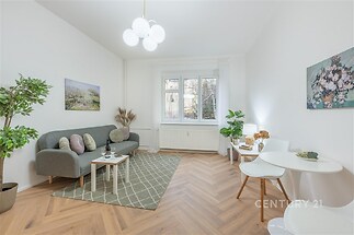 Světlý obývací pokoj s parketovou podlahou, velká okna, moderní design, pohodlná sedací souprava, světlé stěny a dekorativní rostliny