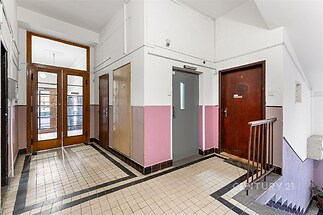 Chodba bytového domu se dlažbou, dřevěnými dveřmi a vintage styl, nabízí příjemnou atmosféru a pohodlný přístup k bytovým jednotkám.