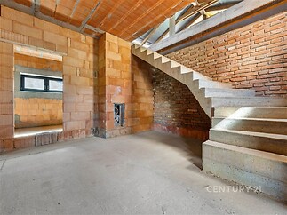 Prázdný interiér s betonovými schody, cihlové stěny a betonová podlaha, připravený k rekonstrukci, nabízí velký potenciál pro moderní bydlení.