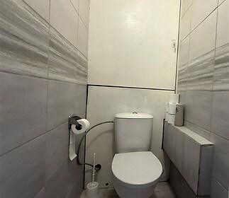 Úzká koupelna s moderní dlažbou na stěnách, bílým toaletním zařízením a decentním větráním, vhodná pro rekonstrukci.
