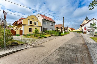 Ulice s rodinnými domy, dlážděný chodník a udržovaná zeleň. Klidná rezidenční čtvrť s tradiční architekturou.