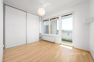 Světlá ložnice s parketovou podlahou, velkými okny a vestavěnými skříněmi, moderní styl a přístup na balkon.