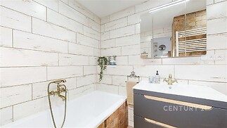 Stylová koupelna s moderními obklady a zlatými armaturami. Prostorná vana a elegantní zrcadlová skříňka poskytují komfort a praktičnost.