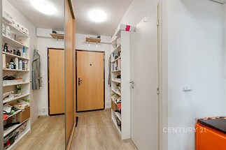 Prostorná předsíň s parketovou podlahou a vestavěnými skříněmi, moderní osvětlení a úložné regály poskytují dostatek úložného prostoru.