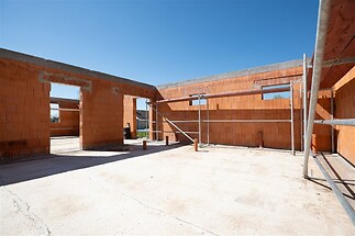 Nezastřešený stavební prostor s cihlovými zdmi, betonovou podlahou a viditelným lešením, vhodný k dokončení moderního domu