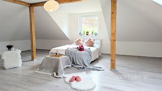 Prostorná ložnice s dřevěnými trámy, světlou laminátovou podlahou a velkým oknem, které poskytuje dostatek přirozeného světla.