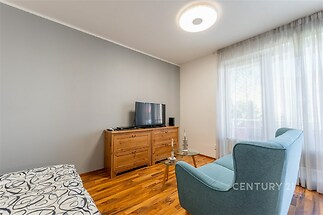 Světlý obývací pokoj s parketovou podlahou, velká okna s průsvitnými závěsy, moderní nábytek a televizní skříňka z přírodního dřeva.