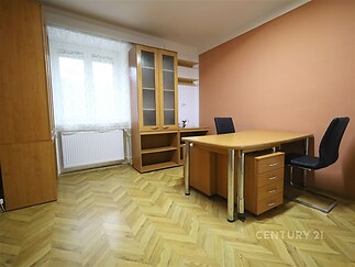 Kancelářský prostor s parketovou podlahou, moderním nábytkem a velkými okny, které zajišťují světlost a vzdušnost místnosti.