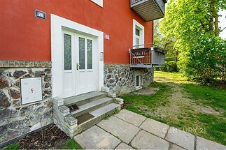 Vchod do bytového domu s kamenným obložením, světlá fasáda a schody vedoucí do zahrady, moderní styl s udržovaným exteriérem.