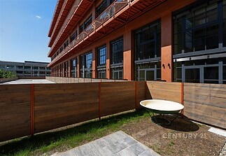 Soukromá venkovní terasa s dřevěným oplocením, moderní architektura, velká okna na budově, slunné prostředí, vhodné pro relaxaci.