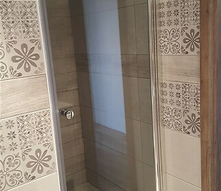 Moderní koupelna s dlažbou a skleněným sprchovým koutem, elegantní obklady s ornamenty, světlý dřevěný rám dveří