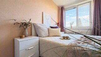 Světlá ložnice s velkými okny, moderním designem a dřevěnými doplňky, dodávající útulnost a komfortní atmosféru pro relaxaci.