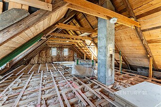 Podkrovní prostor s dřevěnou konstrukcí, připravený k rekonstrukci, s izolací a velkými okny, ideální pro moderní úpravu.