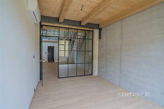 Průmyslově laděná místnost s parketovou podlahou, pohledovým betonem a skleněnými posuvnými dveřmi; moderní styl a klimatizace