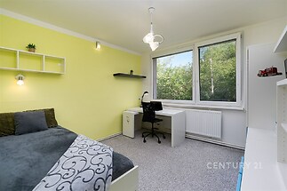Světlý dětský pokoj s velkými okny nabízí moderní design a praktický pracovní stůl. Kobercová podlaha doplňuje útulnou atmosféru.