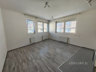 Světlý obývací pokoj s velkými okny, moderní plovoucí podlahou a centrálním vytápěním, ideální pro komfortní bydlení.
