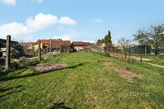 Rozlehlá zahrada s travnatým povrchem, obklopená plotem a stromy, nabízí klidné prostředí u rodinných domů.