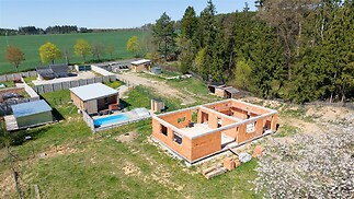 Nedokončená stavba v přírodním prostředí s cihlovými zdmi, prostornou zahradou a stavebními materiály, plánovaná moderní rekonstrukce.