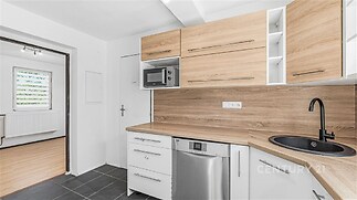 Moderní kuchyň s dřevěnou pracovní deskou, vestavěnými skříněmi a černým dřezem, dlažba na podlaze navozuje elegantní vzhled.