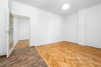 Prázdná místnost s parketovou podlahou a bílými stěnami, která nabízí spojení moderního stylu a dobrého osvětlení, ideální k rekonstrukci.