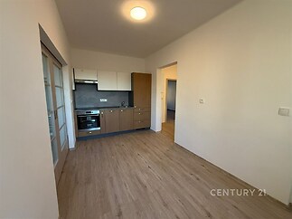 Kuchyňský kout s parketovou podlahou, vestavěnou troubou a moderními skříňkami v světlém interiéru bytové jednotky.