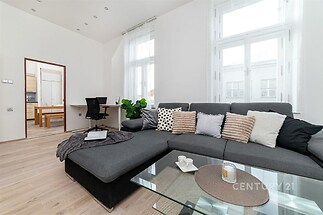 Světlý obývací pokoj s parketovou podlahou a velkými okny, moderní sedací souprava a stylový skleněný konferenční stolek