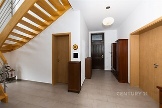 Chodba s dlažbou, moderní interiér, dřevěné schody a dveře, světlé stěny, vestavěná skříň, prostorný design vhodný pro rodinu.