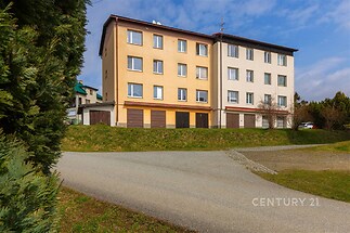 Bytový dům s moderní fasádou, velkými okny a upraveným okolím, nacházející se v klidné rezidenční čtvrti.