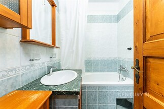 Koupelna s dlažbou a obkladem v modrém odstínu, dřevěný nábytek, moderní umyvadlo a vana s bílým závěsem, světlý interiér.