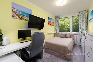 Světlá ložnice s velkými okny nabízí moderní interiér s vestavěným pracovním koutem. Pokoj má světlé zdi a koberec.