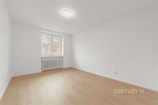 Světlý obývací pokoj s parketovou podlahou, velká okna zajišťují přirozené světlo, moderní styl interiéru.