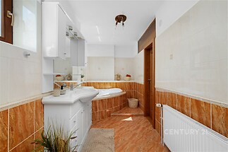 Světlá koupelna s dlažbou, rohovou vanou a vestavěnými skříněmi, moderní vybavení a kvalitní materiály, klidná atmosféra pro relaxaci.