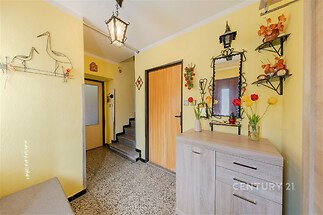 Chodba s dlažbovou podlahou, dekorativní osvětlení, žluté stěny a dřevěná komoda vytvářejí útulný a světlý vstupní prostor.
